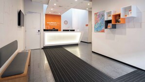 A hotel reception area with a reception desk, a clock, and a seating area with a bench.