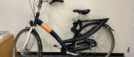 Una bicicleta estática con manillar de marca y asiento negro, apoyada contra una pared en una habitación con suelo de baldosas.