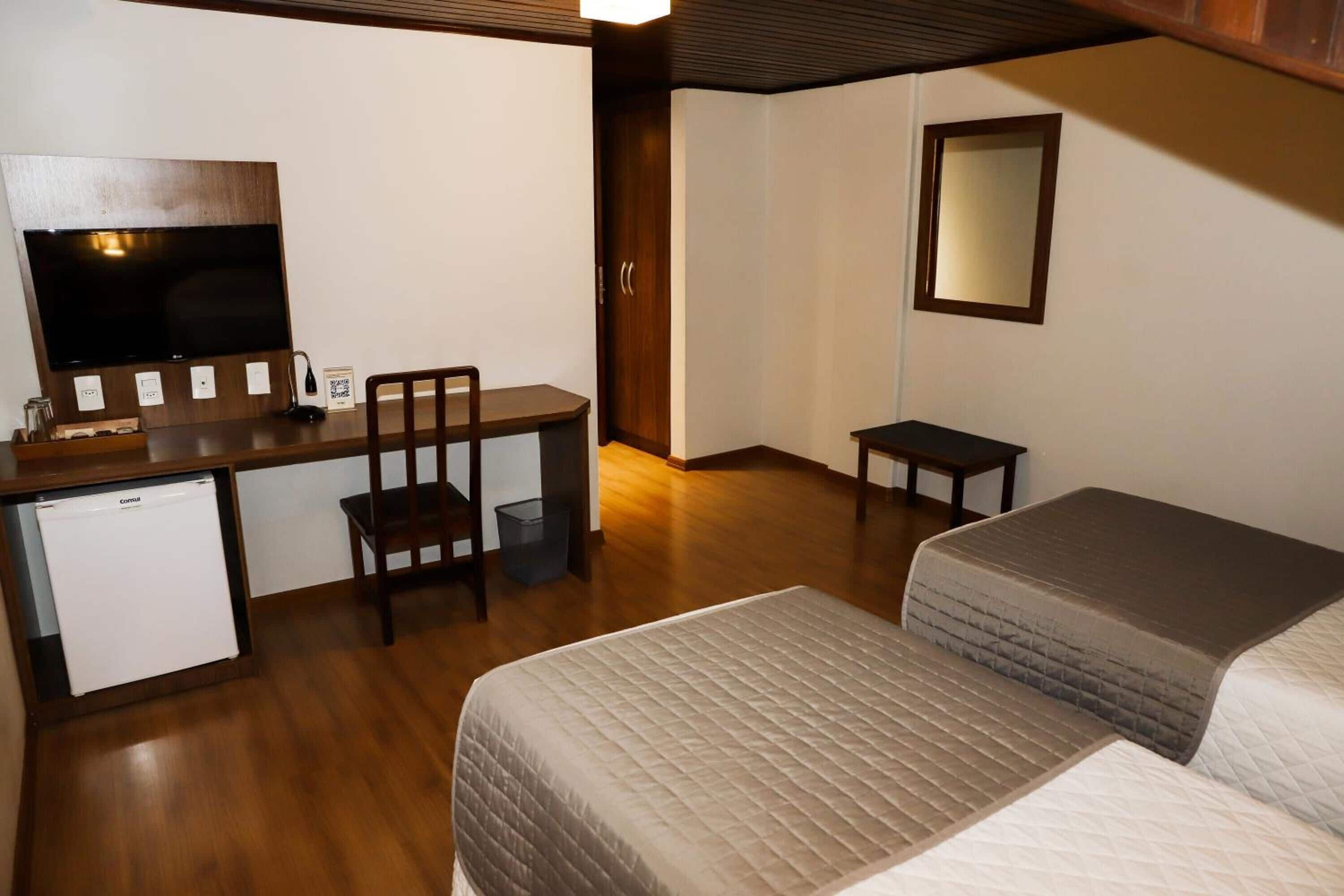 A hotel room with a bed, a desk with a television, a small table, and a chair.