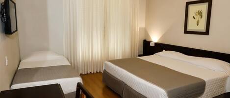 A hotel room with two beds, a desk, a chair, an air conditioner, a curtain, a framed picture on the wall, and a bedside lamp.