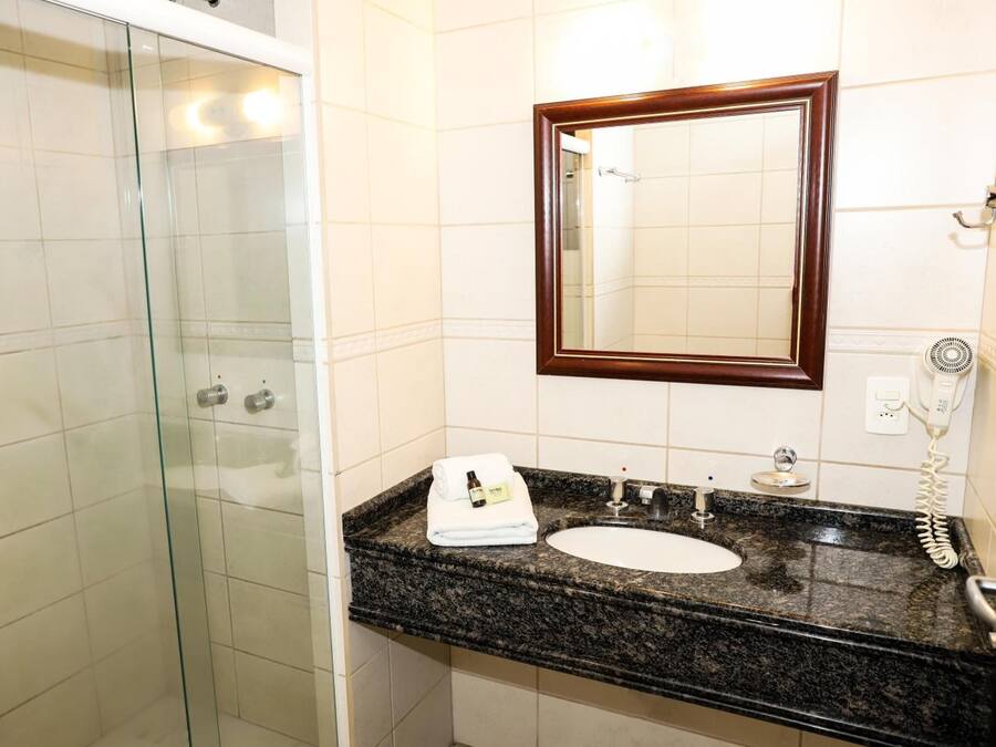 Un baño con cabina de ducha de vidrio, un lavabo con encimera de mármol y un espejo con marco de madera.