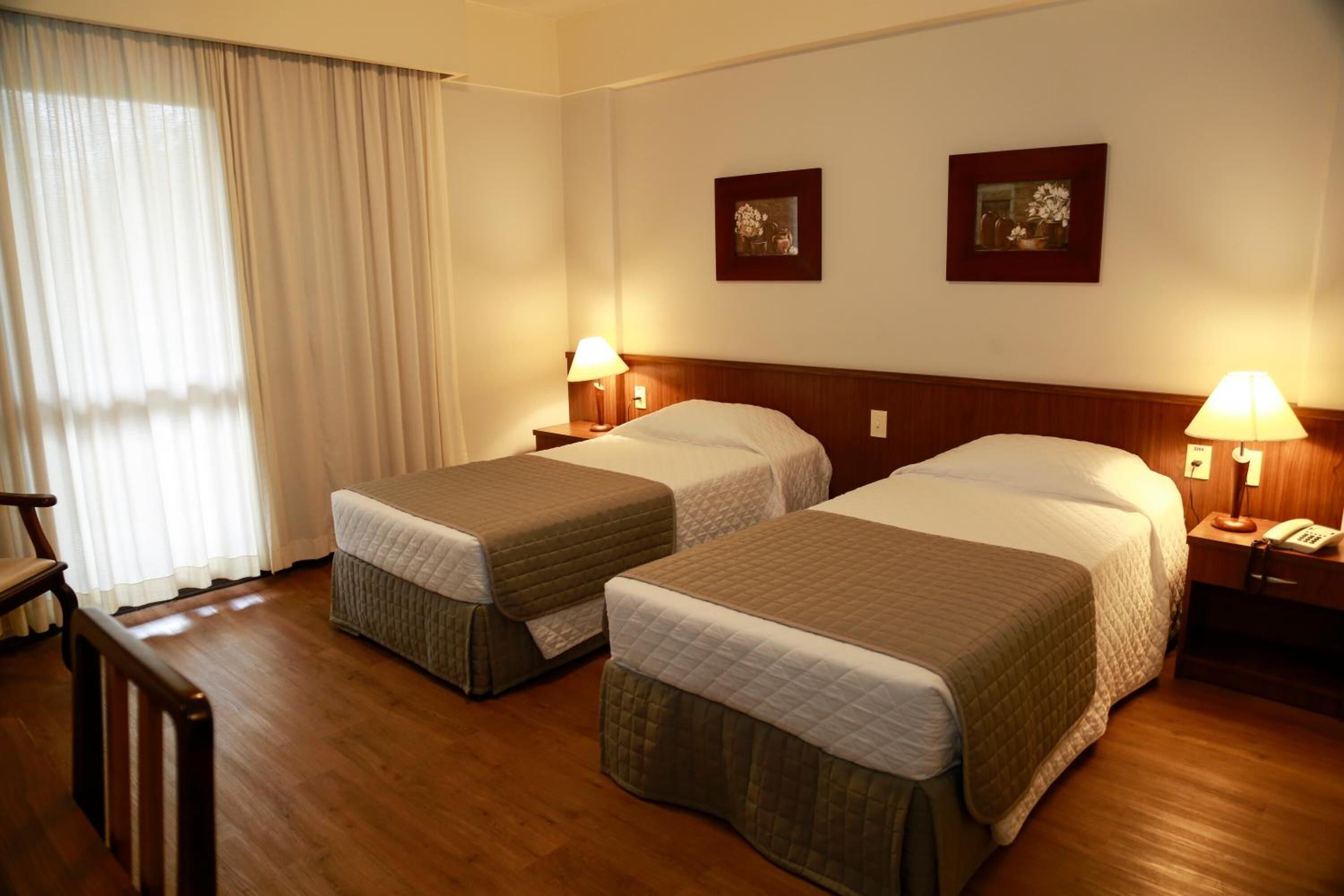 Habitación de hotel con dos camas individuales, cabeceros de madera, lámparas de noche, un escritorio de madera y una silla.