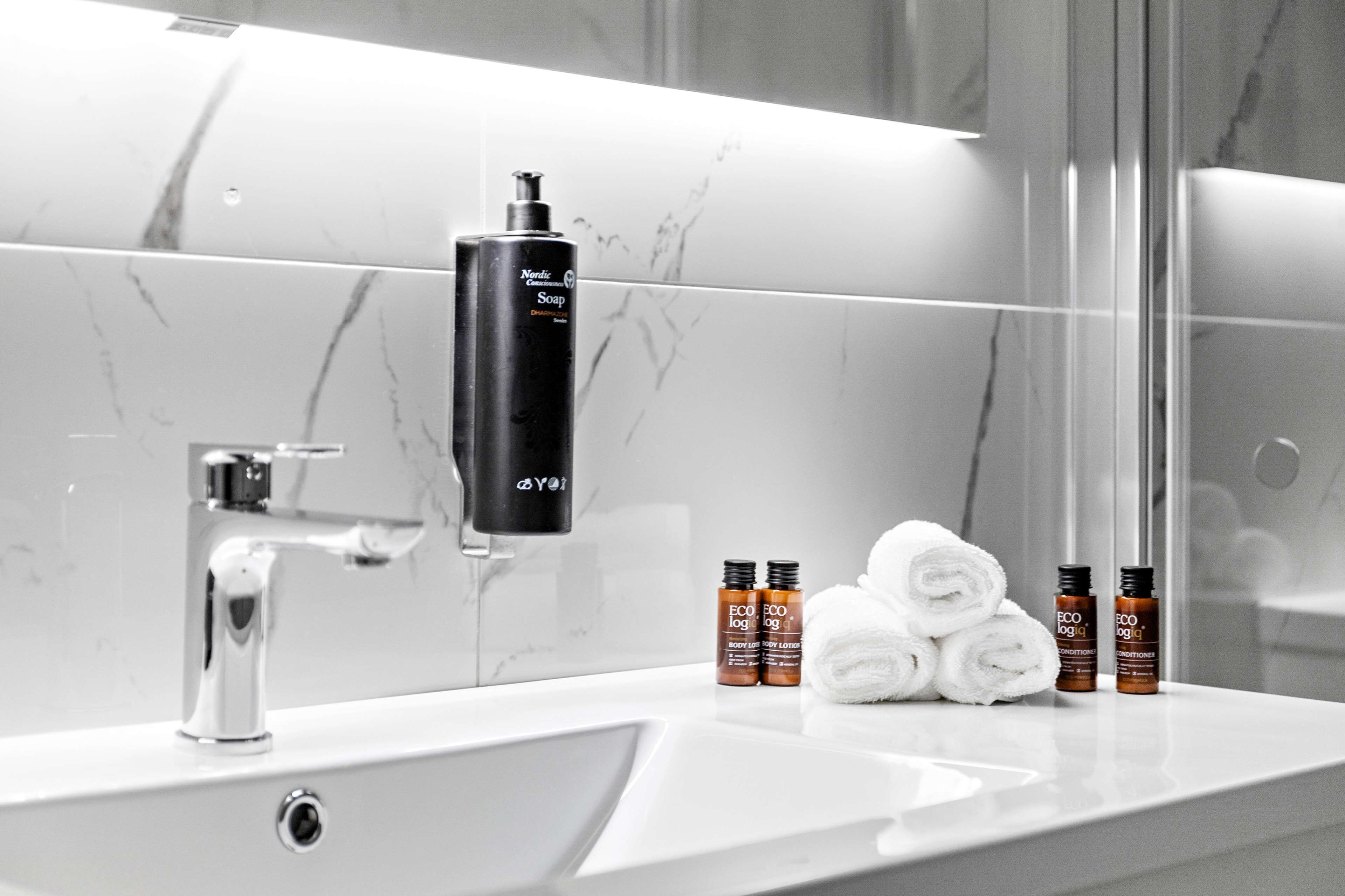 A bathroom with a white sink, a black soap dispenser, and three bottles of ECOlog body lotion.