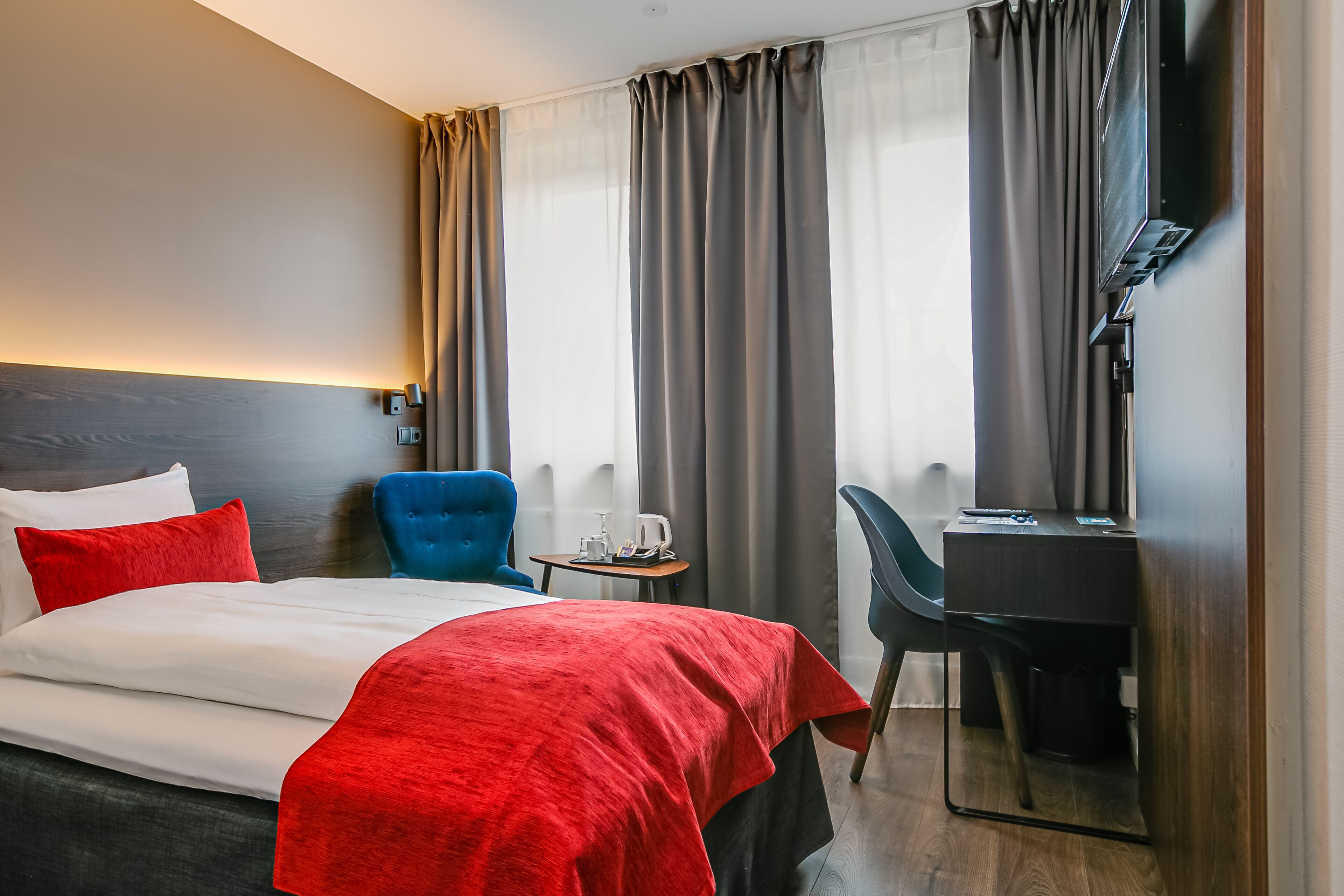 A hotel room with a bed, a desk, a chair, a TV, and curtains.
