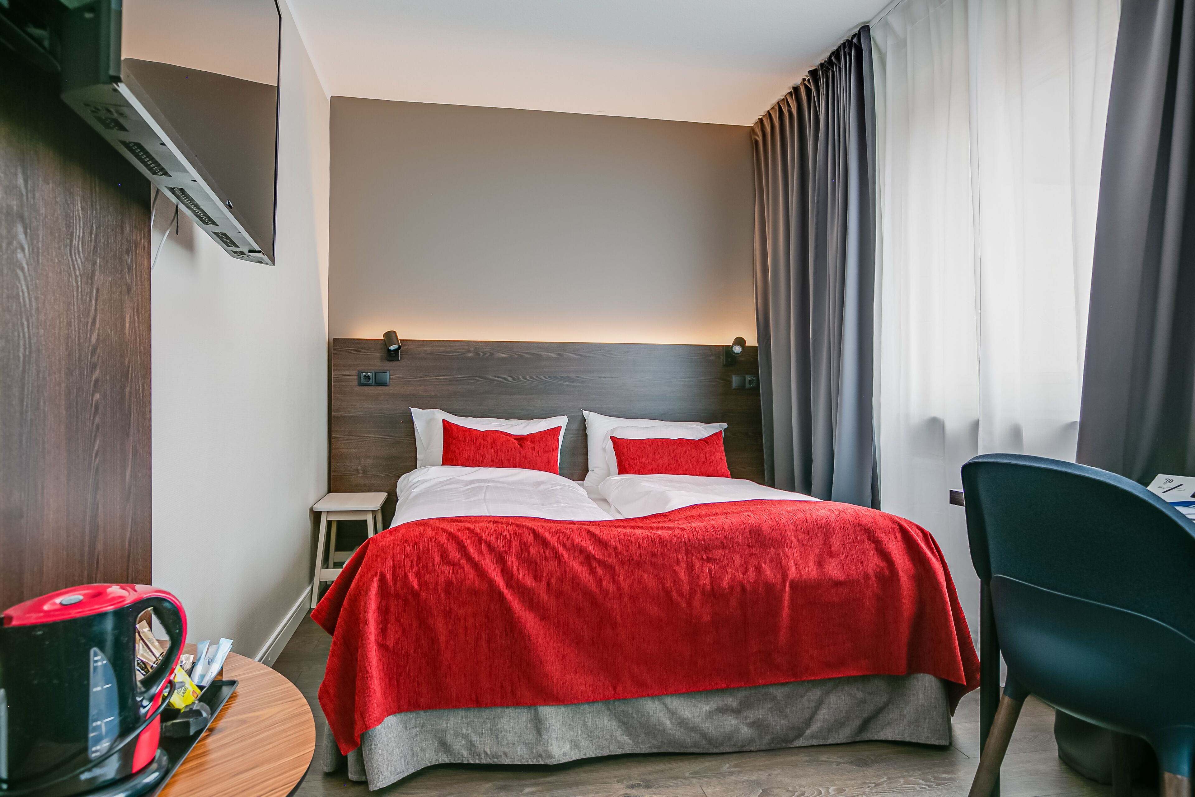 A hotel room with a bed, a desk, a chair, a coffee maker, and a small table.