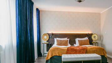 A bedroom with a large bed, two bedside tables, a bench, a chandelier, and a patterned wall.