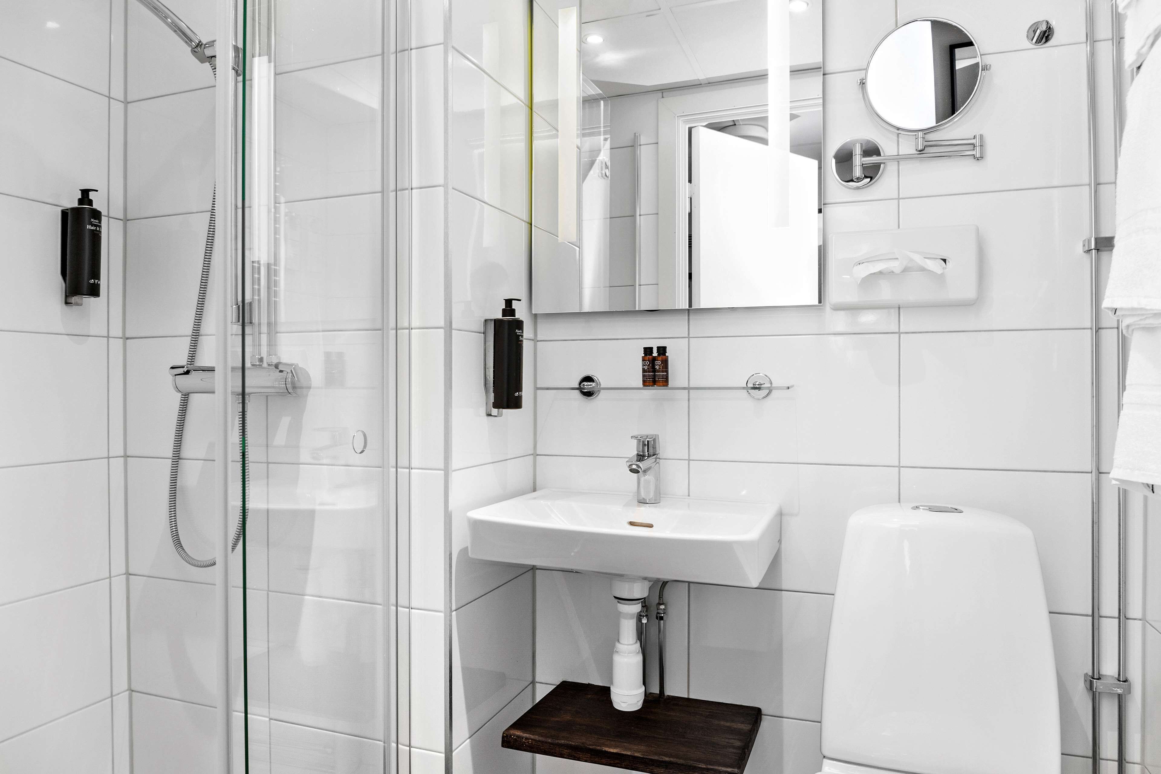 Un baño moderno con ducha de vidrio, un lavamanos blanco y un espejo encima.