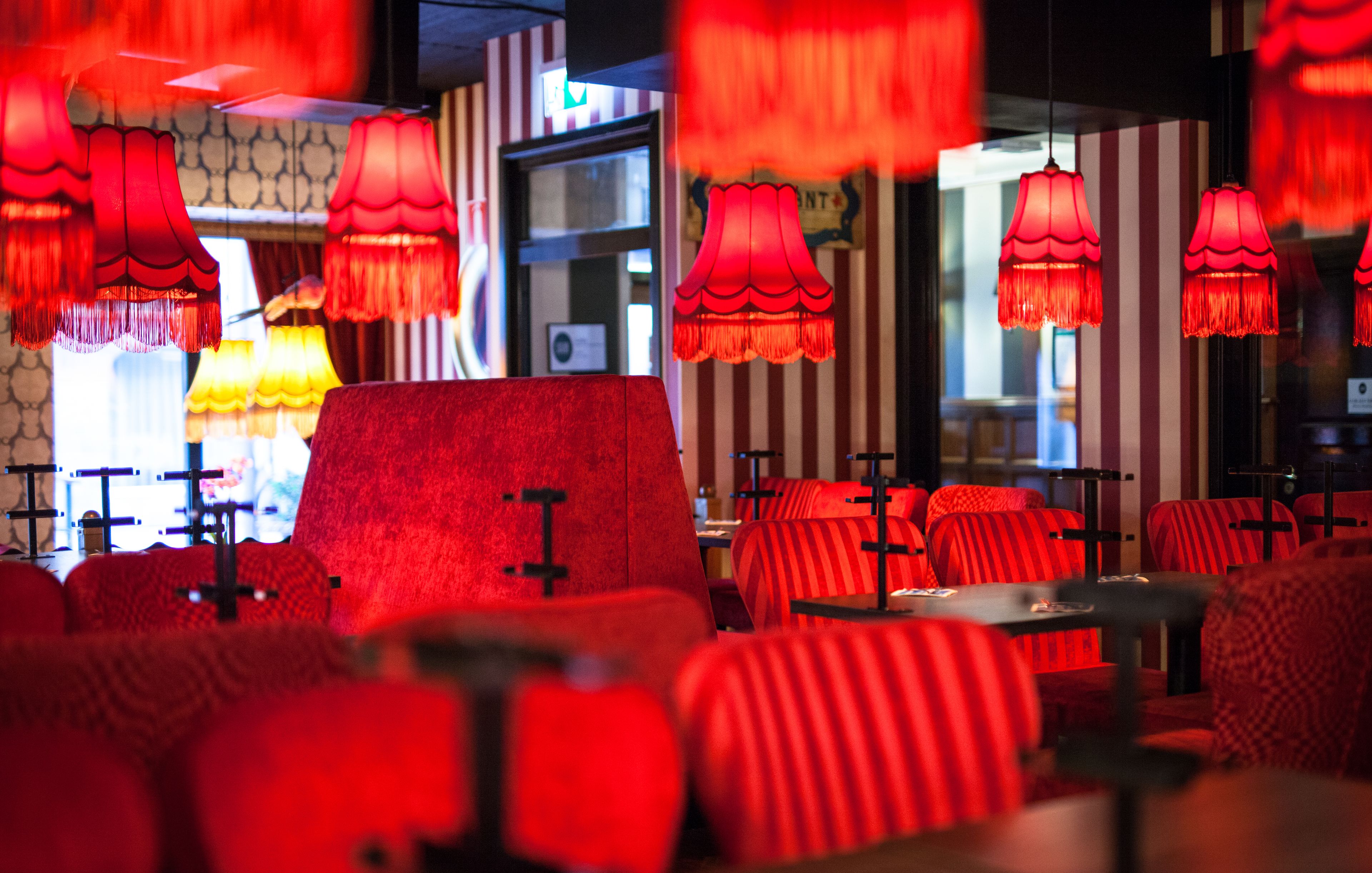Ein Restaurantinneres mit rot gepolsterten Stühlen, gestreiften Wänden und hängenden roten Lampen.