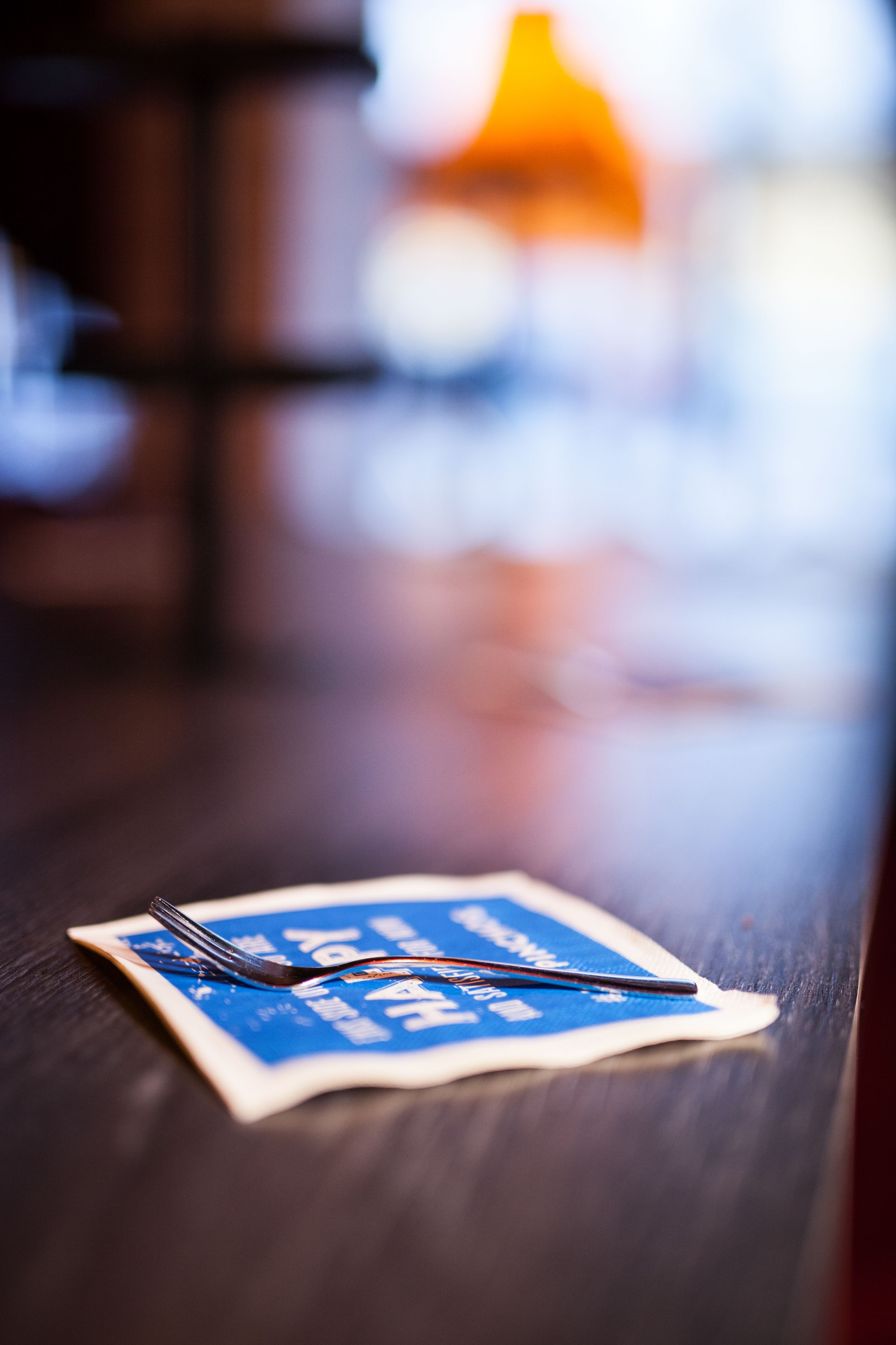 A close-up of a fork and spoon on a napkin with a blue logo, placed on a wooden table.