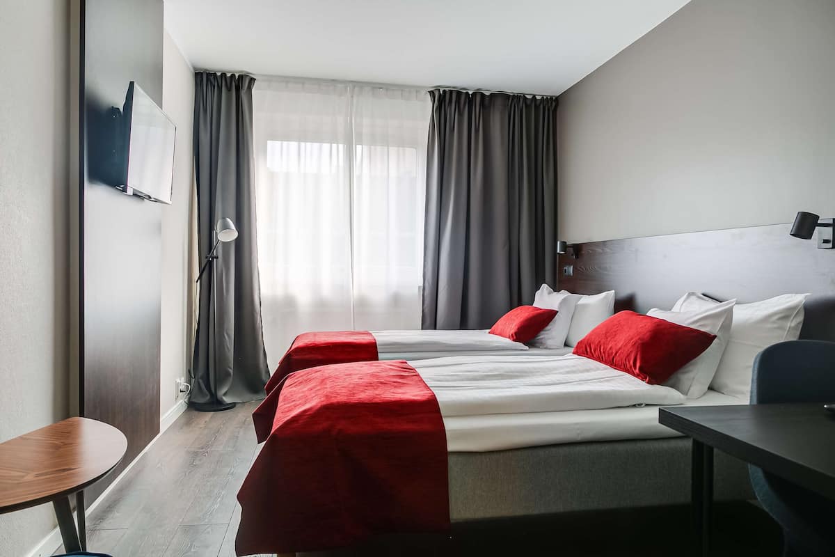 A hotel room with two beds, a TV, a desk, and a chair.