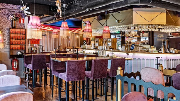 A bar area with purple bar stools, a counter with a variety of glassware, and a decorative ceiling with hanging lamps. - Best Western Hotel Savoy (Karlstad)