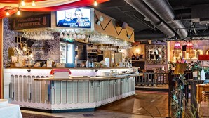 A bar area with a counter, hanging glasses, and a television screen displaying a show. - Best Western Hotel Savoy (Karlstad)