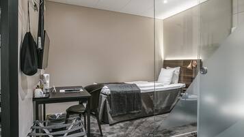 A modern hotel room with a bed, a desk, a chair, and a glass partition.