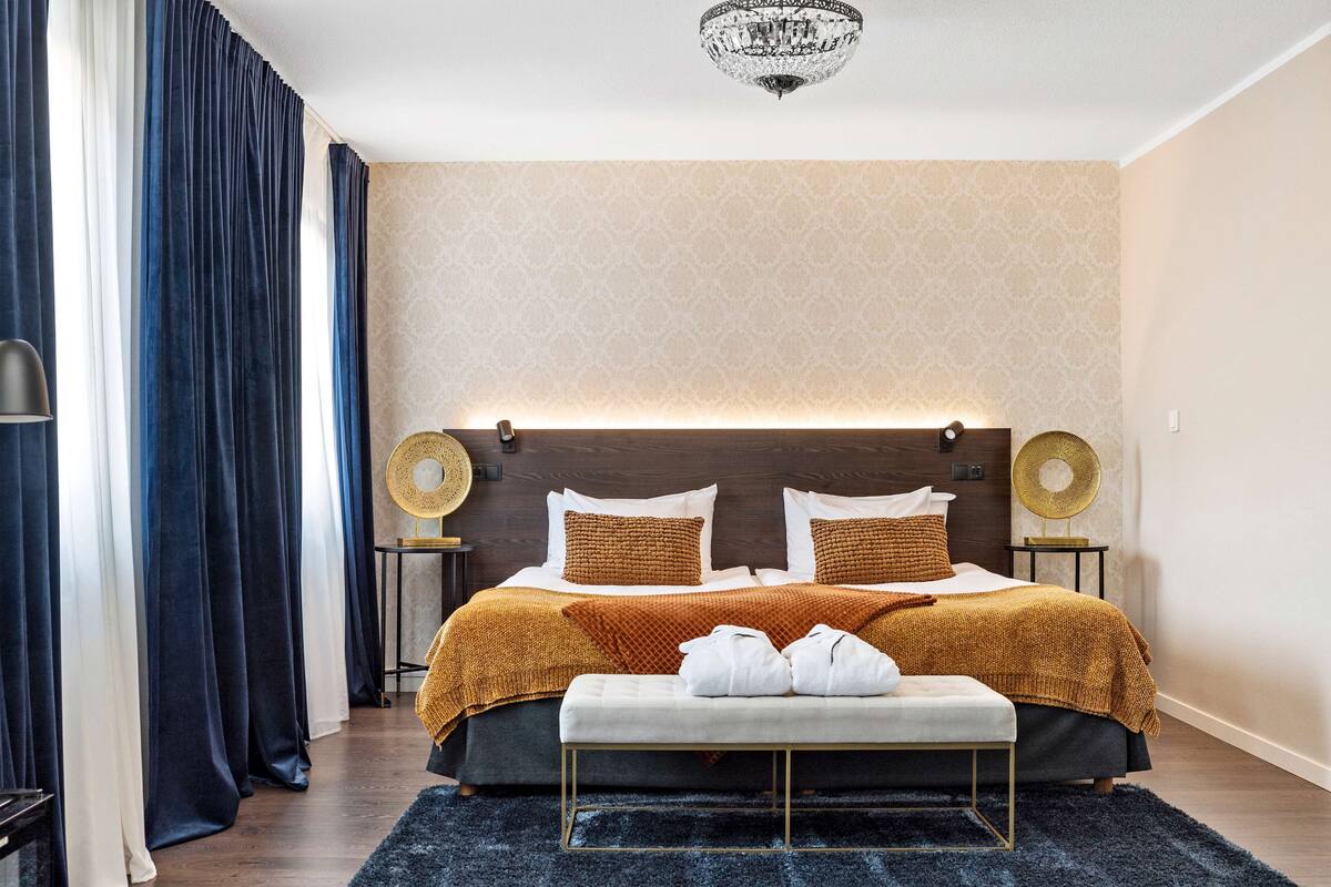 A modern bedroom with a large bed, two bedside tables, a bench, and a chandelier.