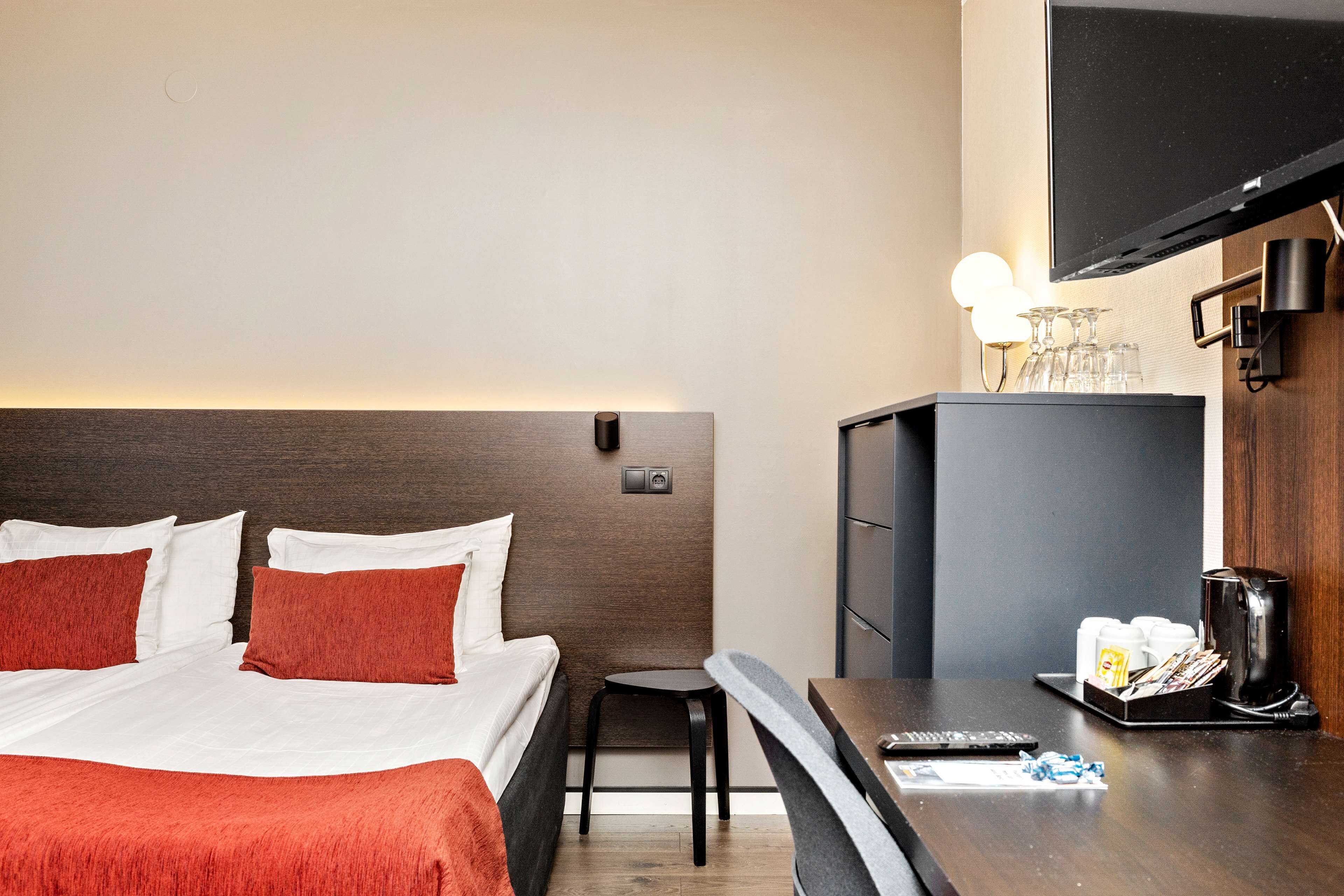 A hotel room with a bed, a small table, a TV, and a minibar.