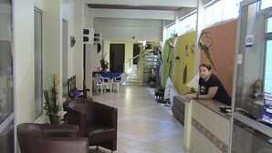 A reception area with a receptionist, a sofa, a dining area, and a staircase in the background. - Pousada Porto Belo (Ipojuca)