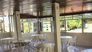 An indoor patio area with several round tables and white plastic chairs. - Pousada Porto Belo (Ipojuca)
