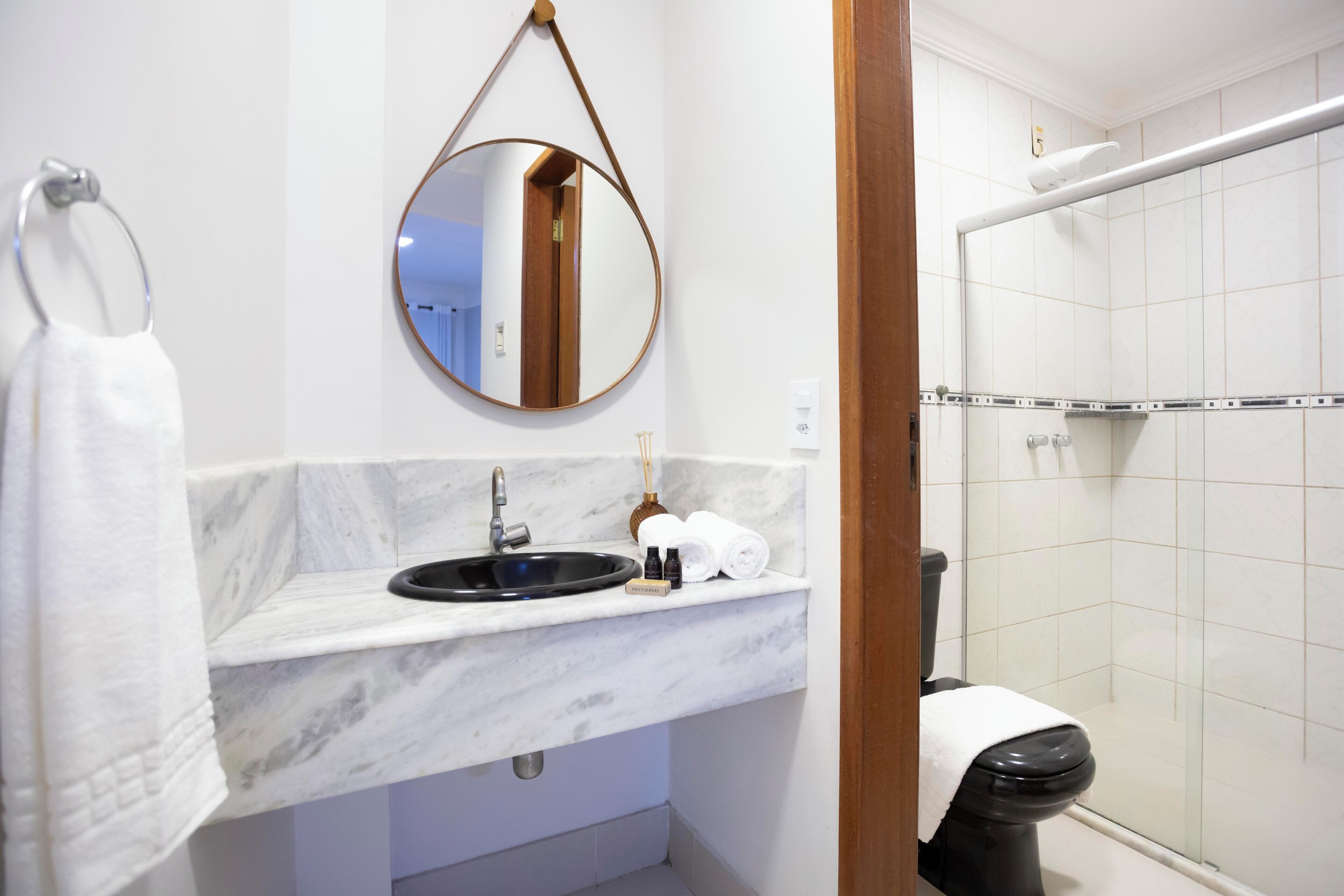 A bathroom with a marble sink, a round mirror, a toilet, and a shower area.
