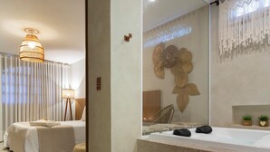 A modern bedroom with a large bed, a bedside table, a mirror, and a small seating area. - Pousada Timoneiro (Vila Velha)