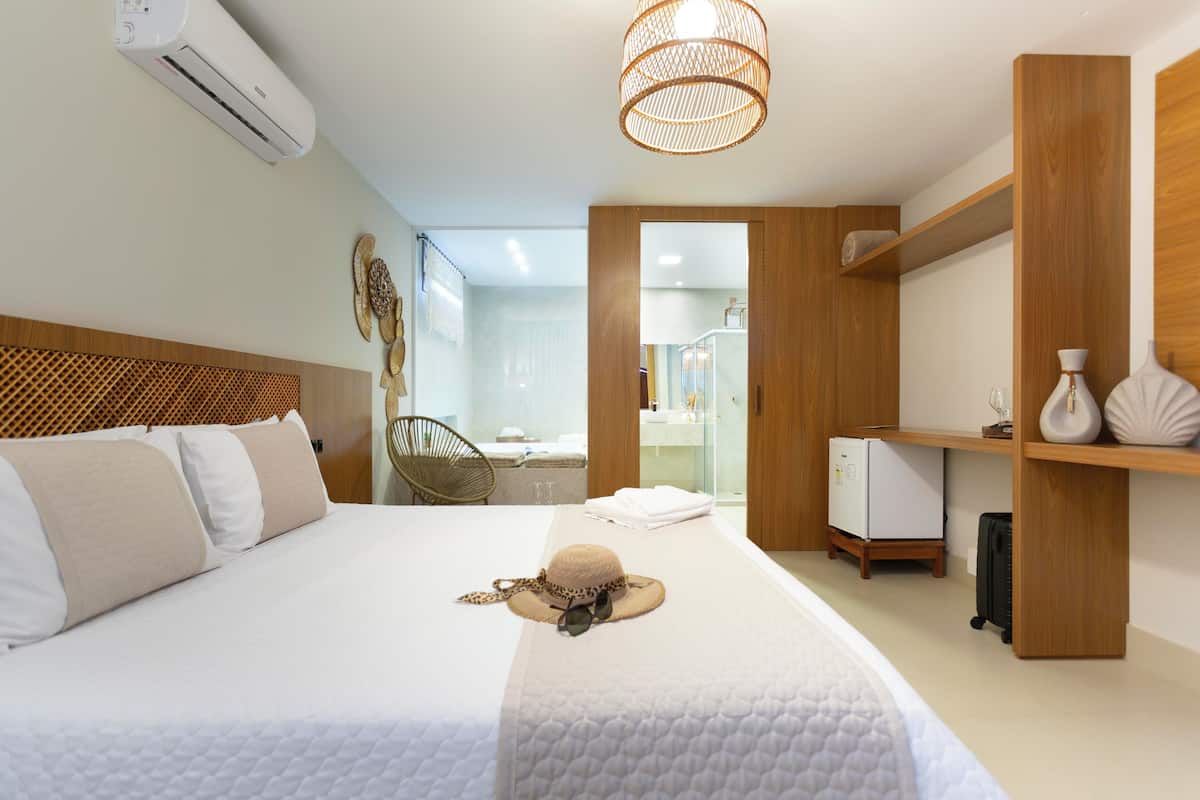A hotel room with a bed, a wardrobe, a desk, a chair, and a bathroom visible through an open door.