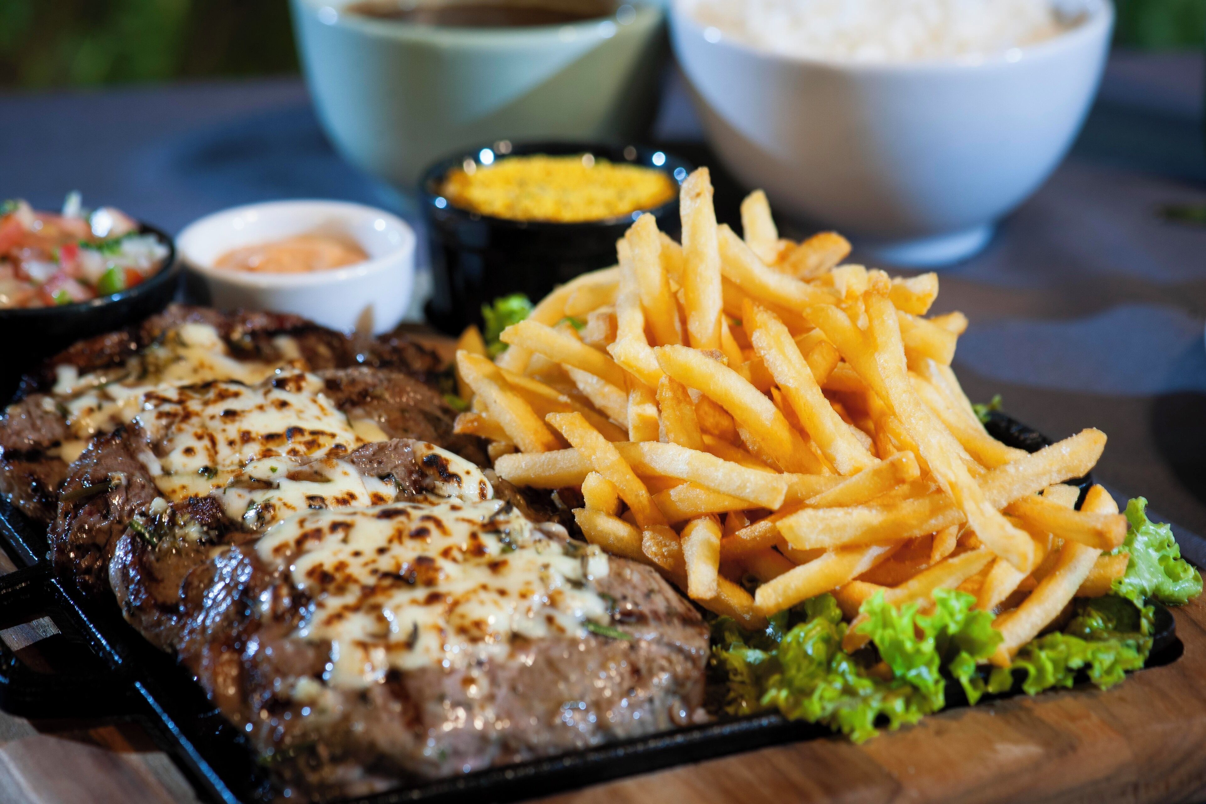 Un plato con bistec a la parrilla, papas fritas y una ensalada como guarnición sobre una tabla de madera.