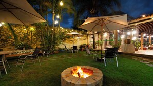 An outdoor patio area with tables and chairs, a fire pit, and string lights. - Pousada Timoneiro (Vila Velha)