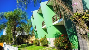 A green building with a modern design, surrounded by lush greenery and palm trees. - Pousada Timoneiro (Vila Velha)