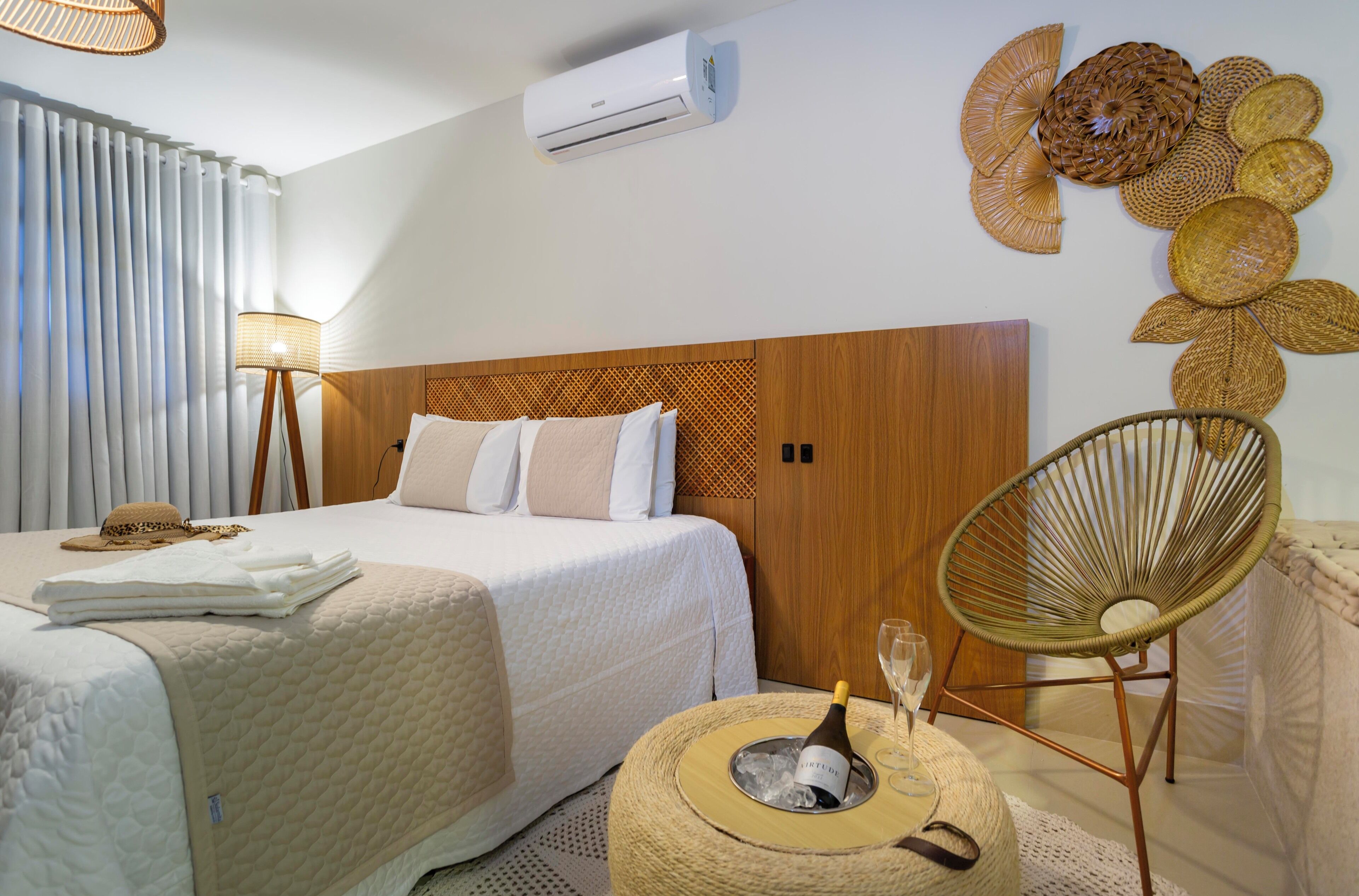 Habitación de hotel con cama, lámpara de noche, una silla de mimbre, aire acondicionado de pared y un adorno mural.