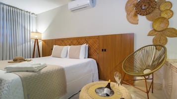 Habitación de hotel con cama, lámpara de noche, una silla de mimbre, aire acondicionado de pared y un adorno mural.