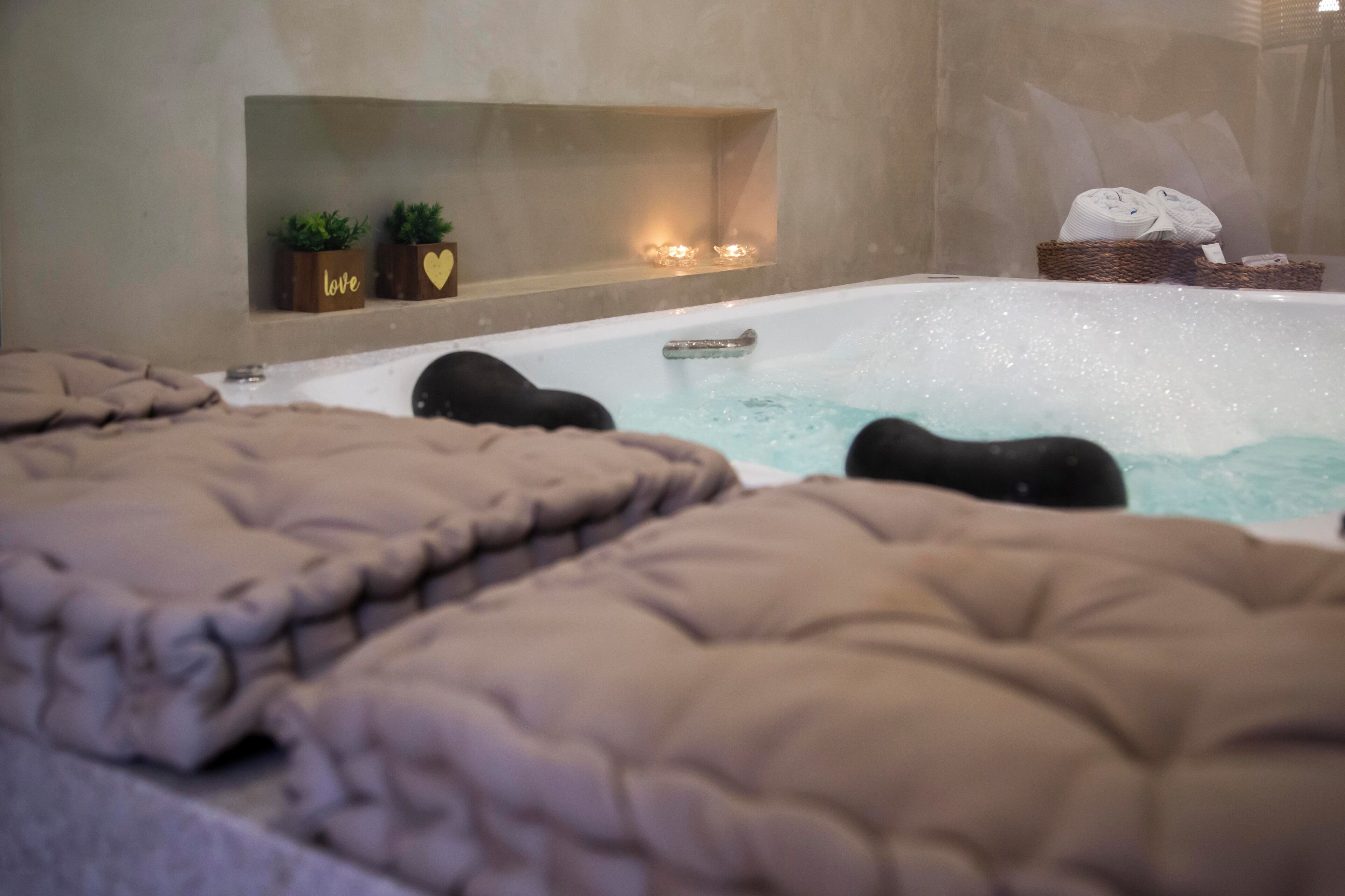 A spa room with a hot tub, two plush towels, and a shelf with plants and candles.