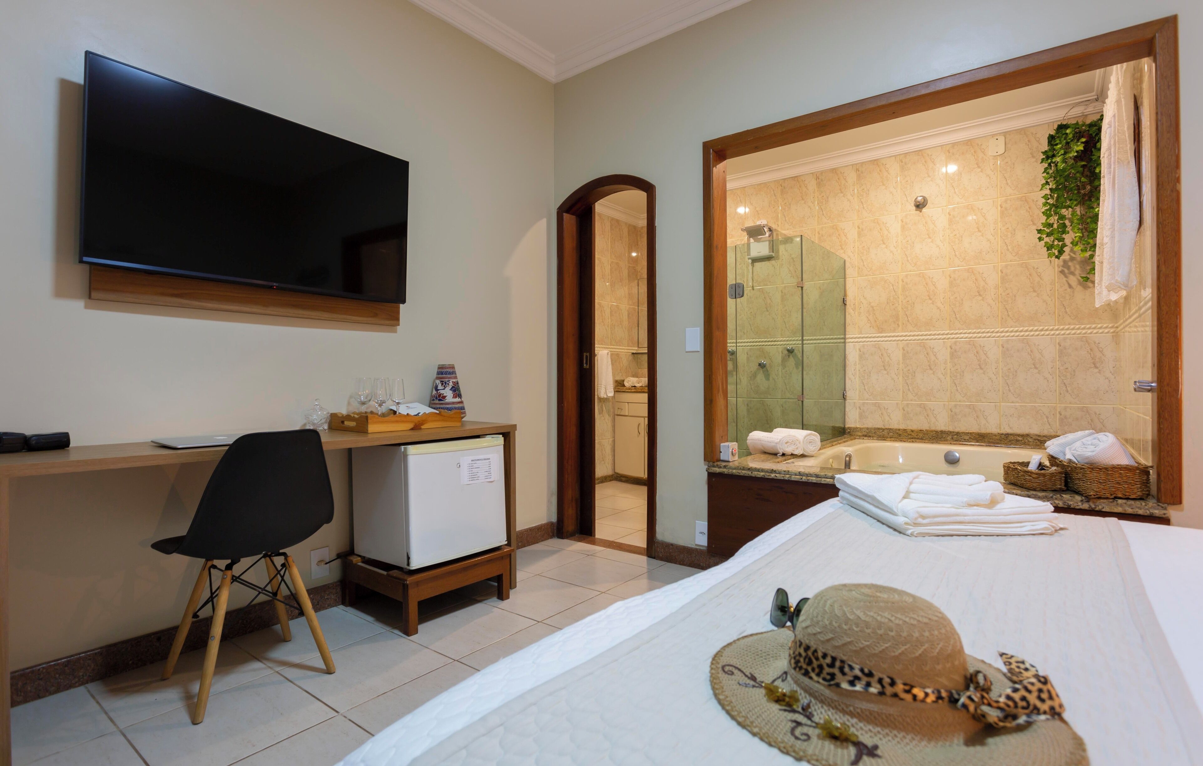 Habitación de hotel con televisor, escritorio, silla y cama con toallas y un sombrero.