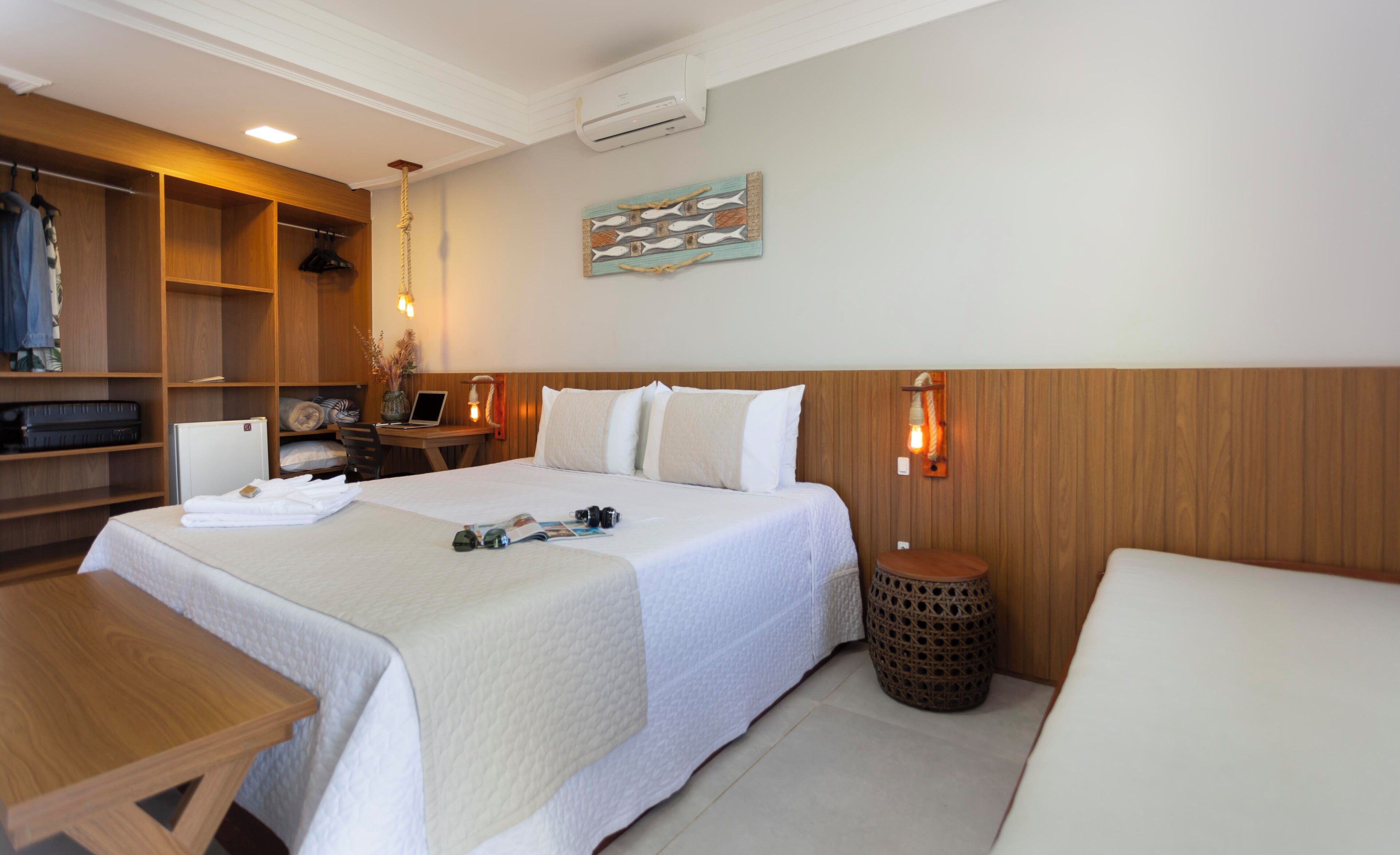 A hotel room with a bed, a desk, a chair, a small table, a wardrobe, and a wall-mounted artwork.