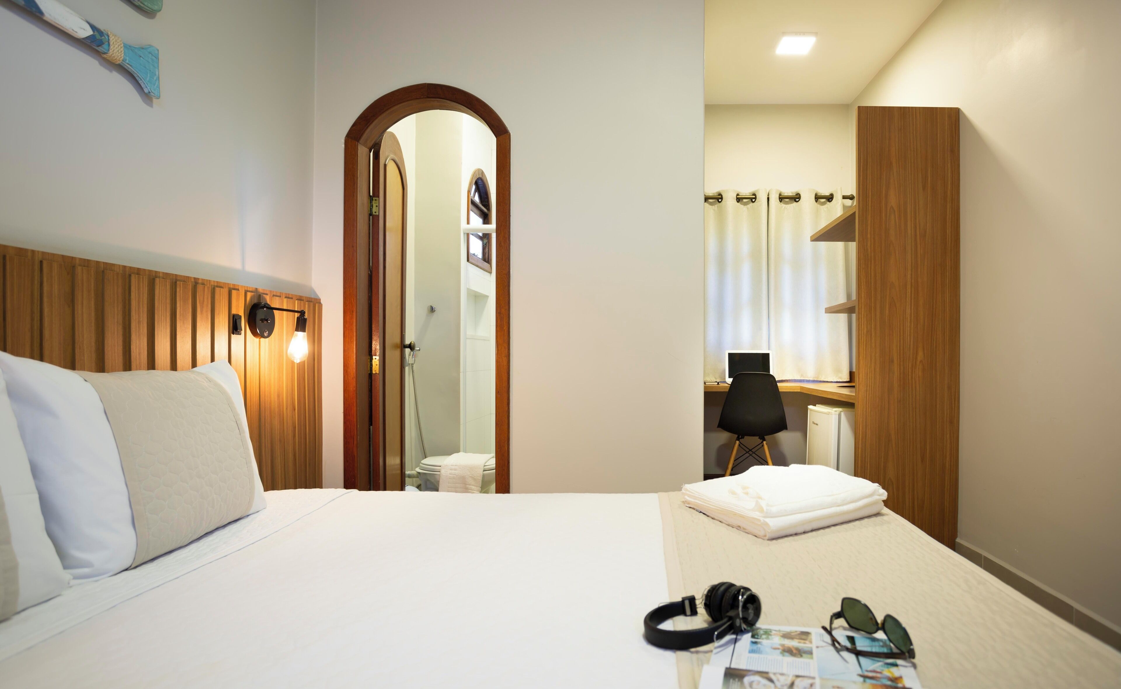 A hotel room with a bed, a desk with a computer, a mirror, and a shower area.