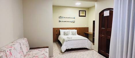 Un dormitorio con cama, sofá floral, escritorio de madera y una puerta con un cartel.