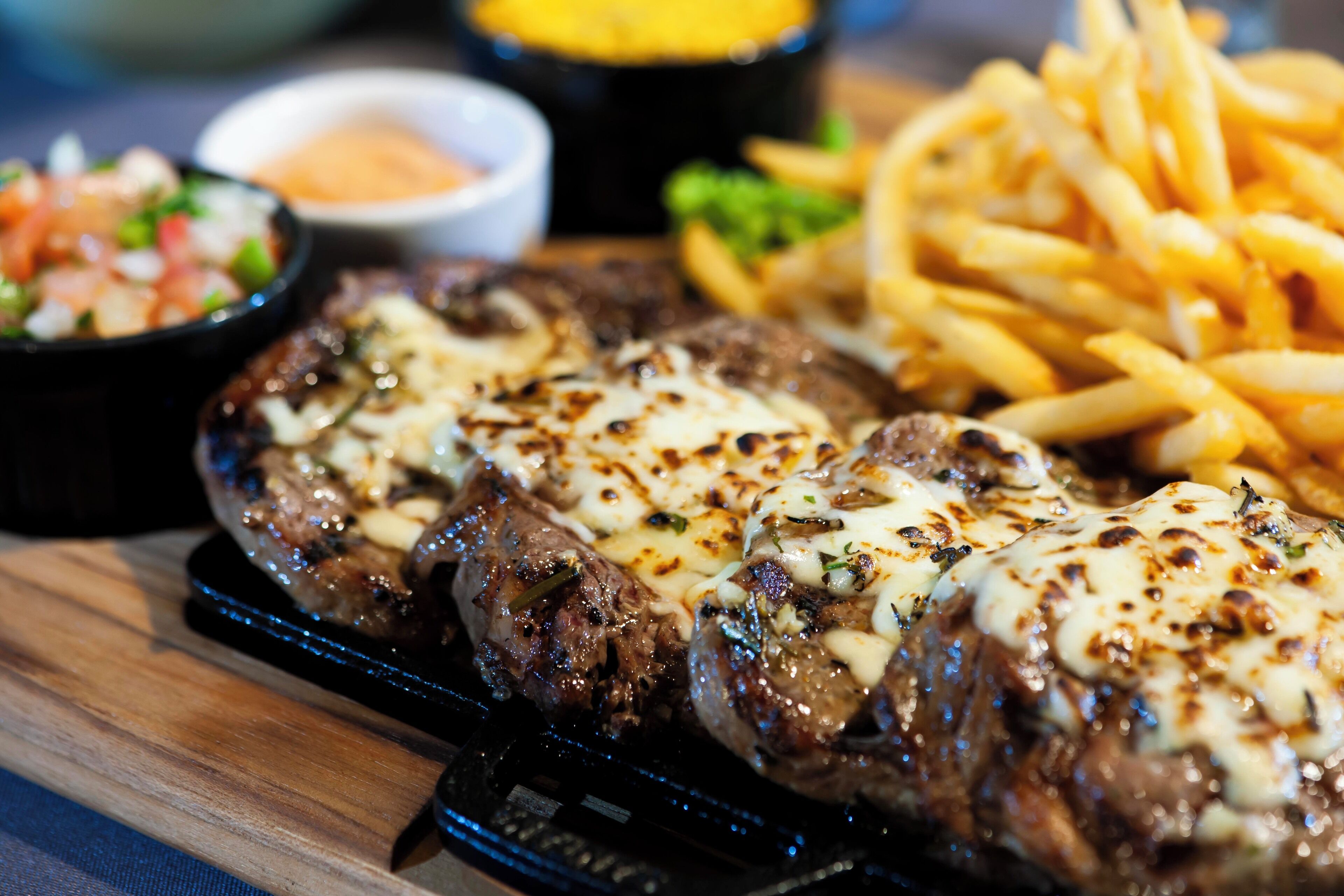 Grillezett steak, ráolvasztott sajttal, egy tálon, mellé hasábburgonya és egy kisebb saláta.