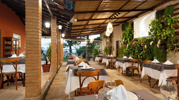 A restaurant with tables set for dining, a brick column, and a wall with greenery. - Pousada Timoneiro (Vila Velha)