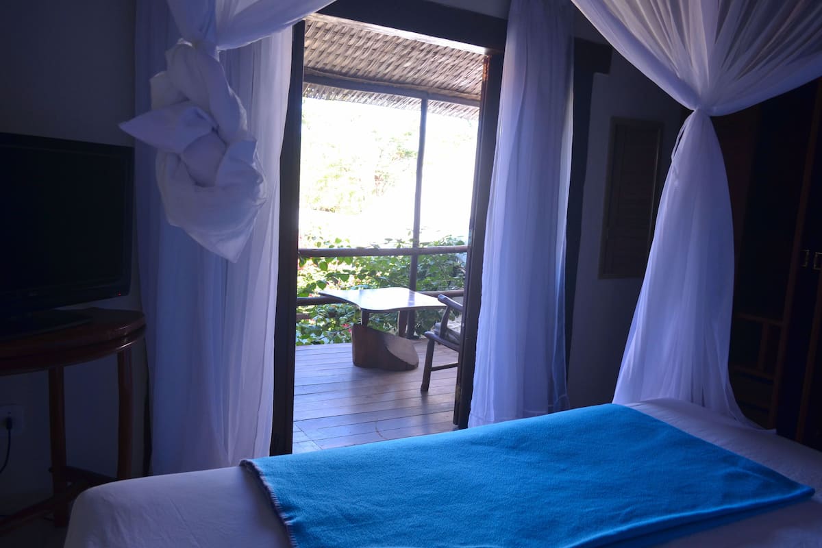 A bedroom with a bed, a television on a stand, and a balcony with a table and chairs.