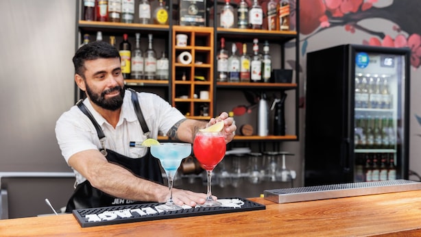 A bartender at a bar with a keyboard and a drink in front of him. - Hotel Miramar (Balneário Camboriú)