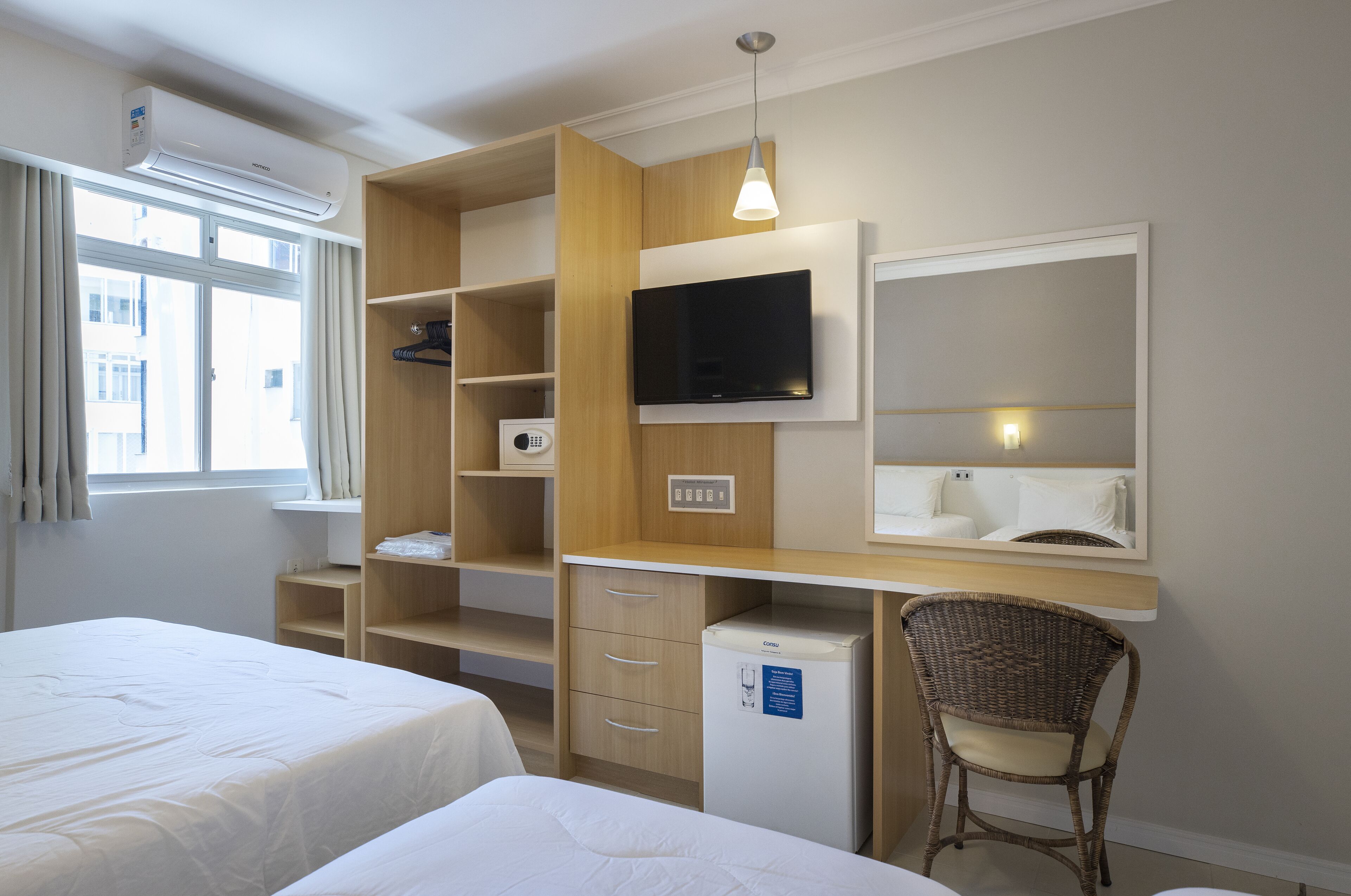 A hotel room with a bed, a desk, a television, and a refrigerator.