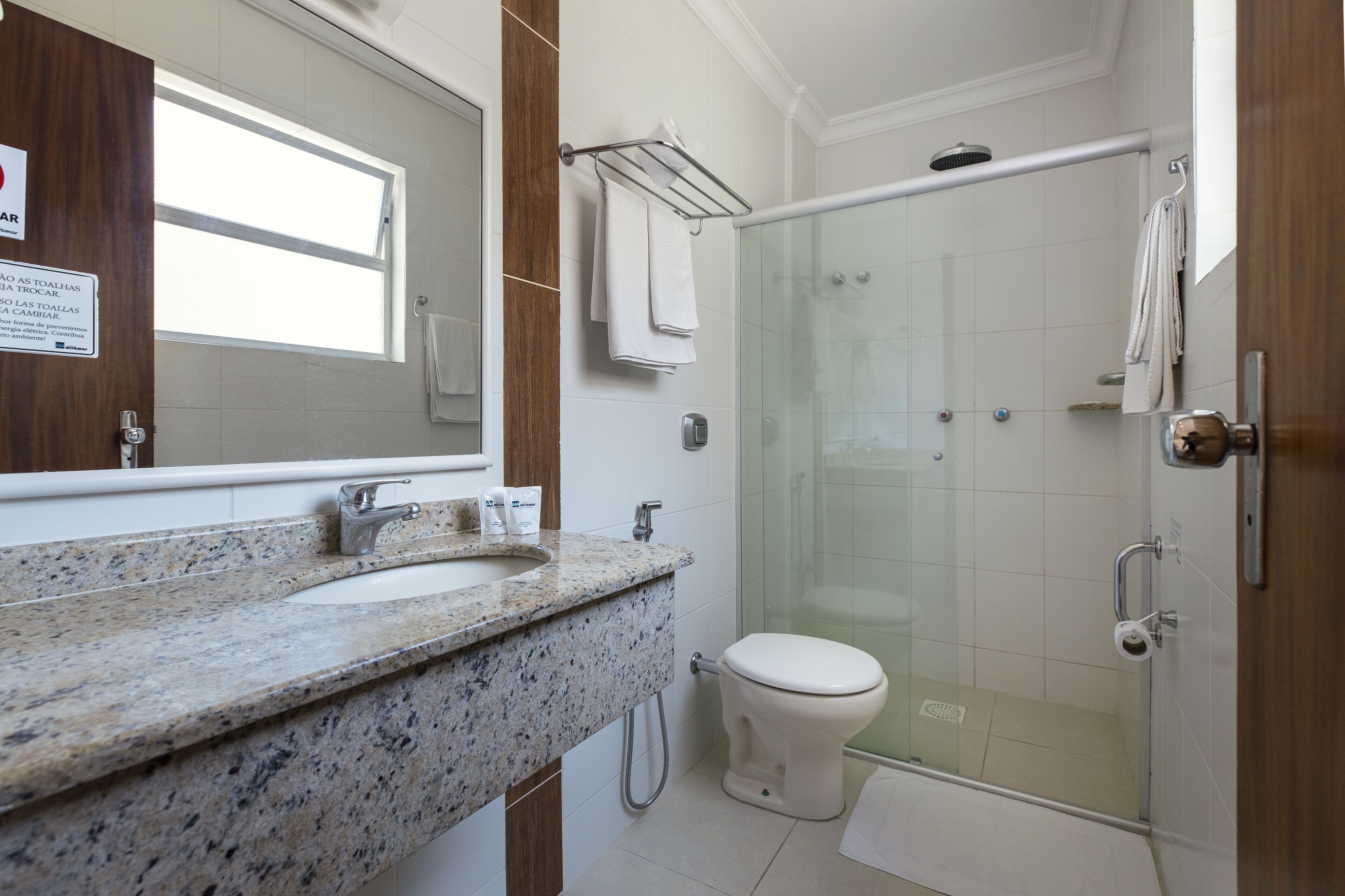 A bathroom with a granite countertop, a toilet, a glass shower enclosure, and a towel rack.