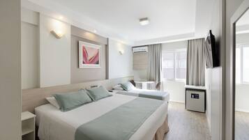 Habitación de hotel con dos camas, un escritorio, una silla, una mesita, un armario y una ventana con cortinas.