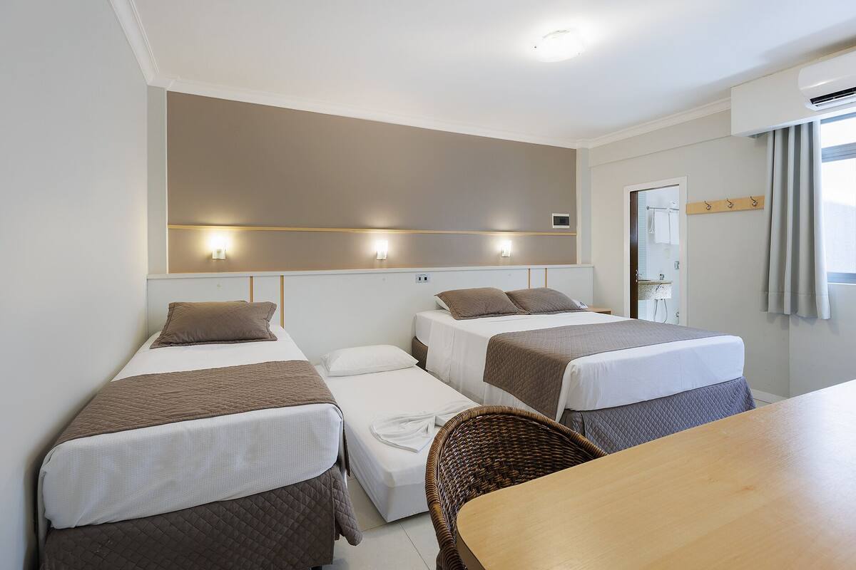 A hotel room with two single beds, a wooden table, and a wicker chair.