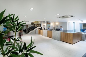 A modern reception area with a staircase, reception desk, and a large potted plant.