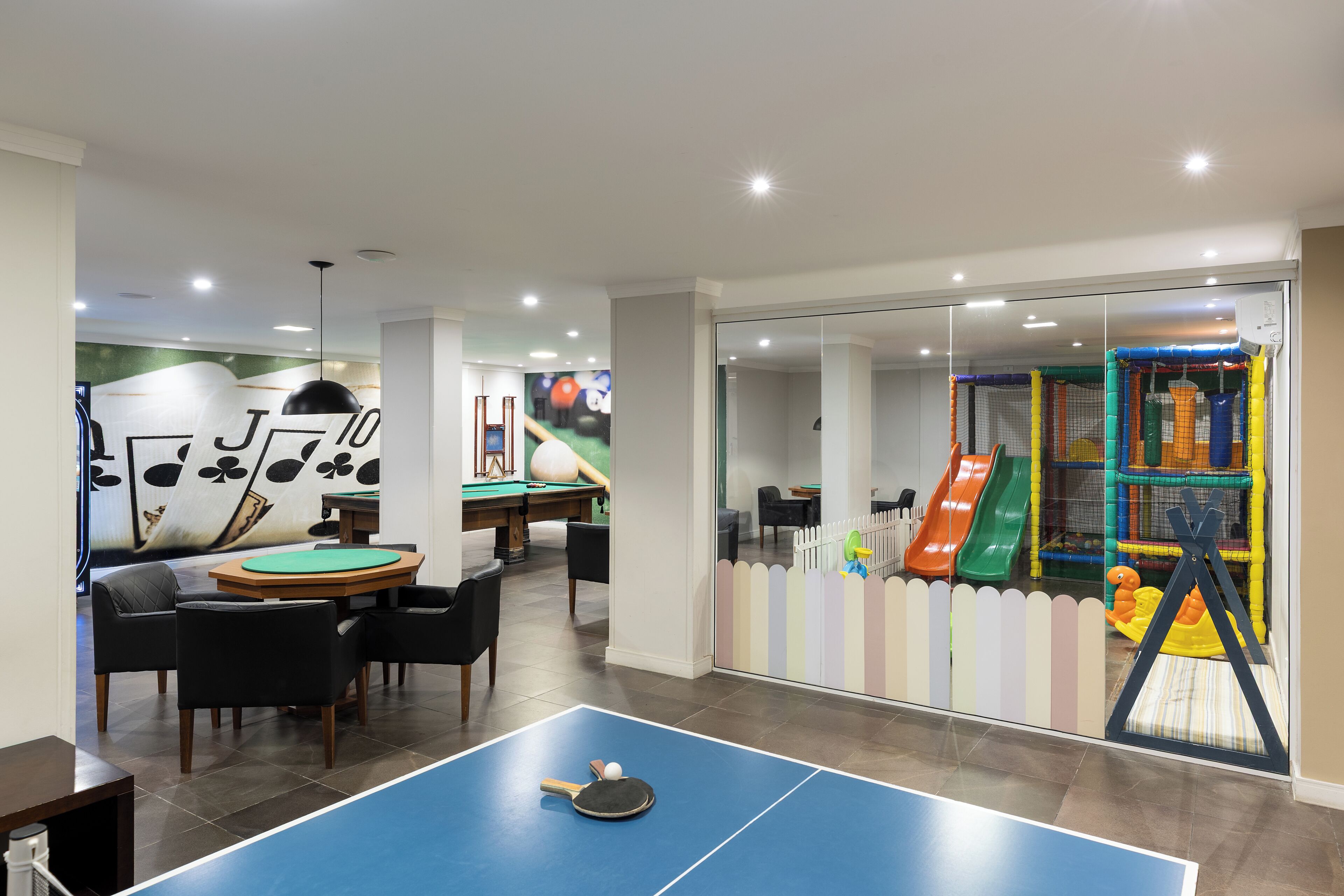Una habitación con mesa de billar, sillas, mesa de ping pong y zona de juegos infantiles con toboganes y una red de escalada.