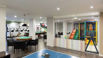 Una habitación con mesa de billar, sillas, mesa de ping pong y zona de juegos infantiles con toboganes y una red de escalada.