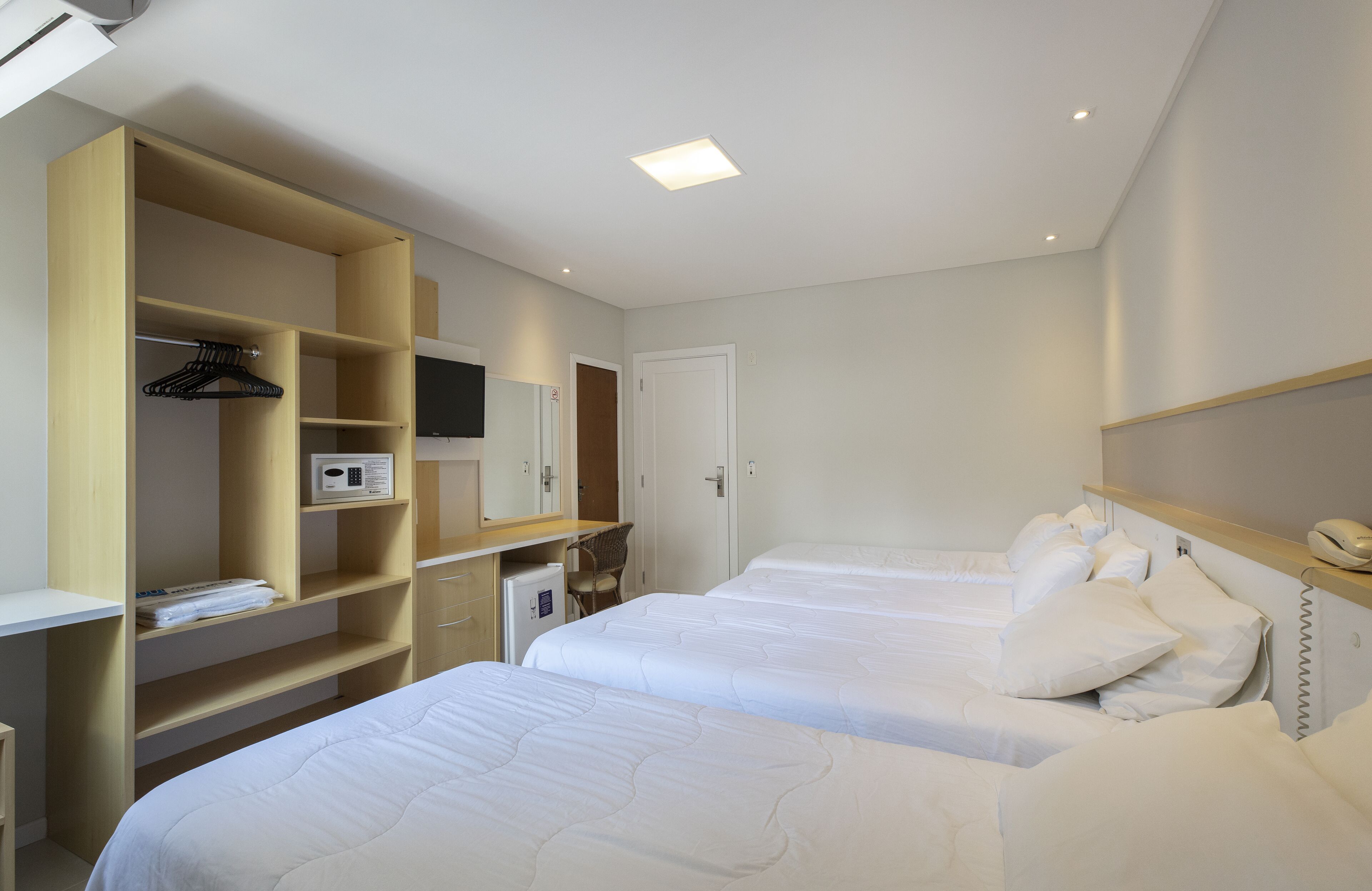 Een hotelkamer met twee bedden, een bureau met stoel, een kledingkast, een televisie en een kleine koelkast.
