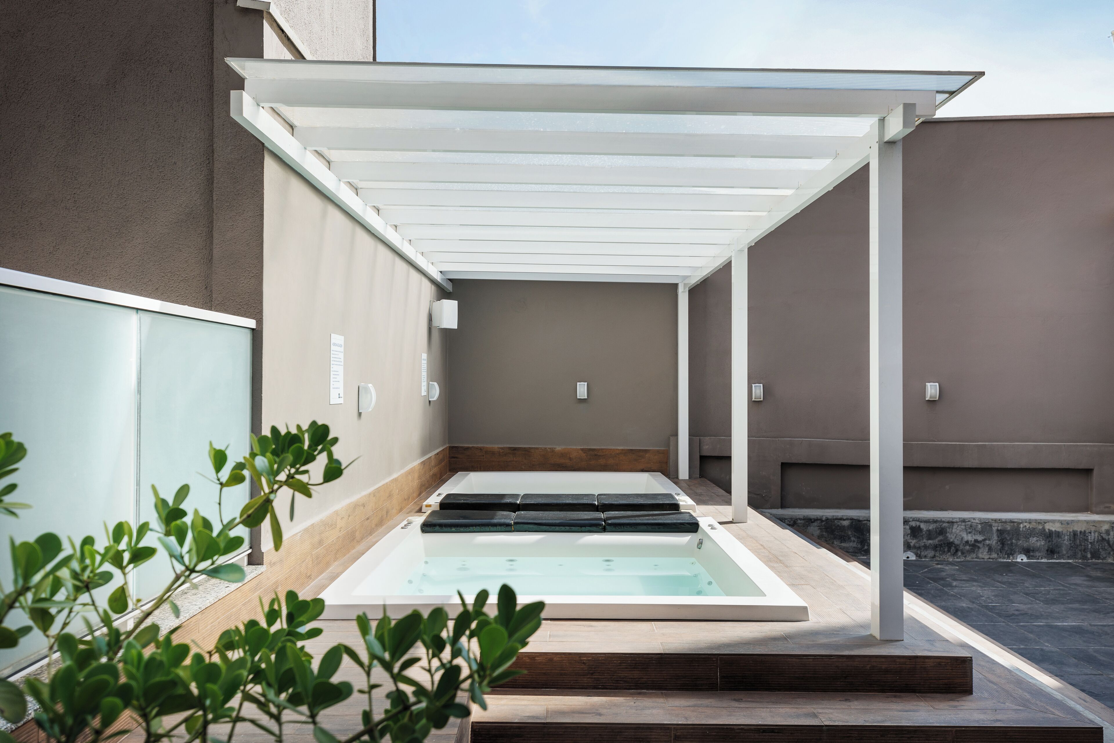 Un espace de détente avec un jacuzzi à ciel ouvert, des marches en bois et une pergola blanche.