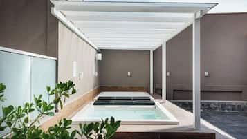 Un espace de détente avec un jacuzzi à ciel ouvert, des marches en bois et une pergola blanche.
