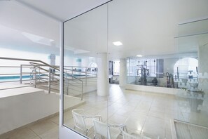A modern indoor swimming pool area with glass walls, a staircase, and exercise equipment.