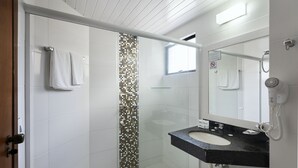 A modern bathroom with a glass-enclosed shower, a white sink with a black countertop, and a large mirror. - Hotel Miramar (Balneário Camboriú)